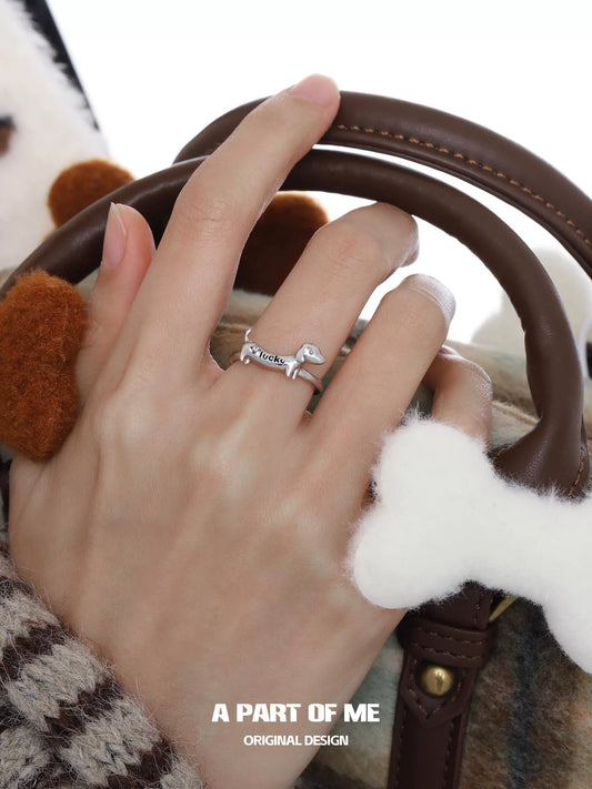 Silver dachshund silver ring worn on a hand holding a stylish handbag with dog bone accessories