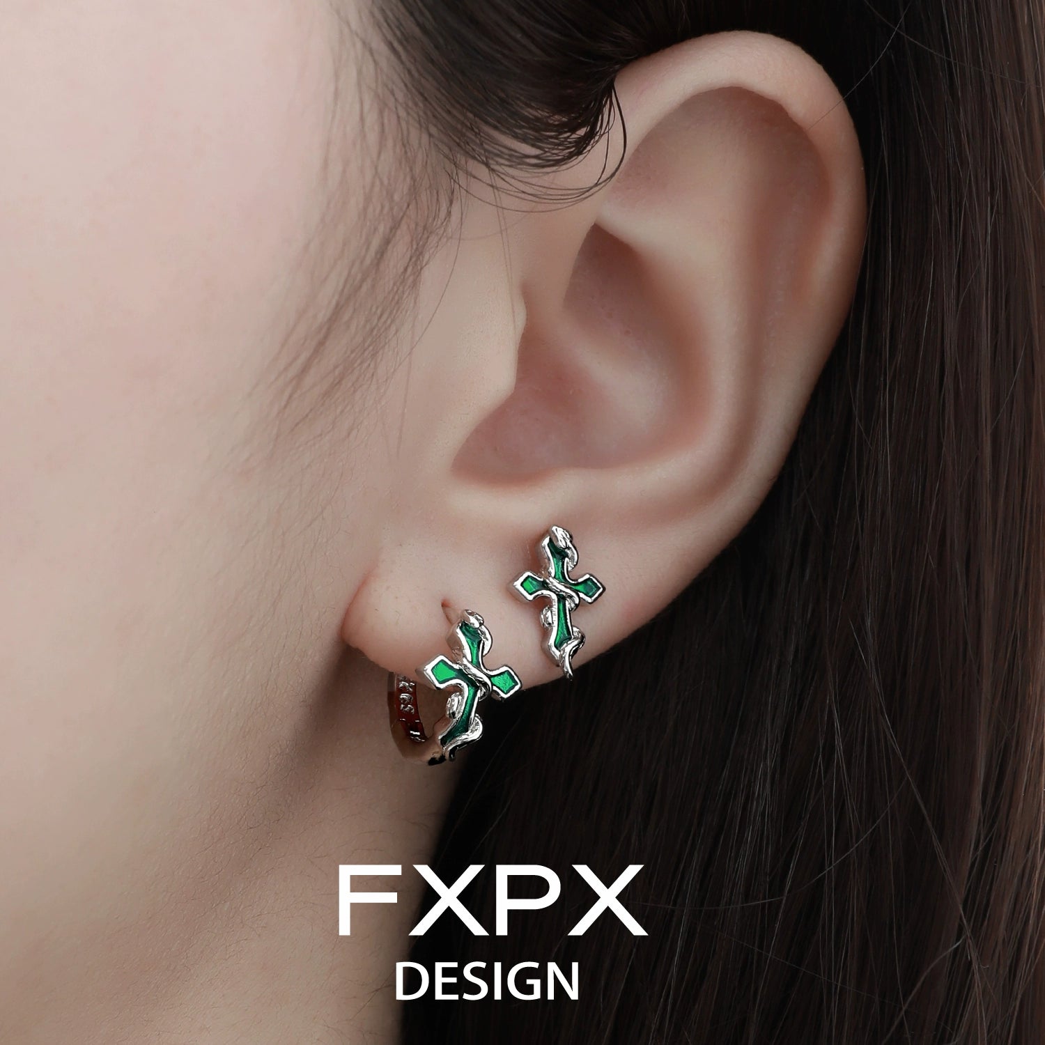 Close-up of bloody doll jewelry Y2K snake cross earrings worn on ear in green and silver design