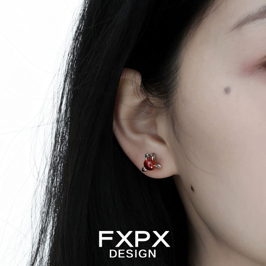 Close-up of bloody dragon claw gothic earrings worn on a person's ear with dark hair