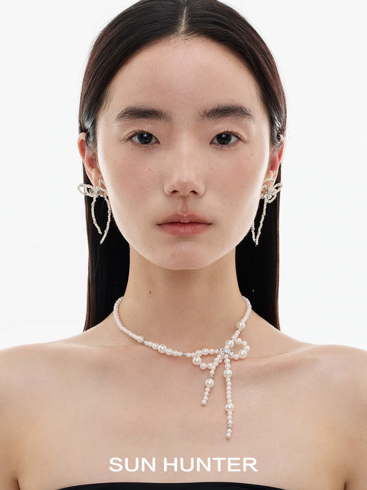 Elegant SUN HUNTER pearl bow ribbon earrings showcased on a model's ears with a simple background