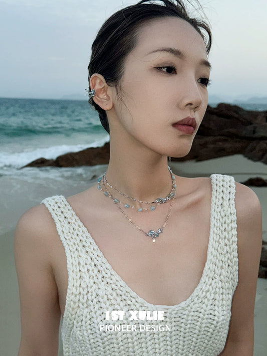 Model wearing a playful fish necklace on the beach with ocean waves in the background
