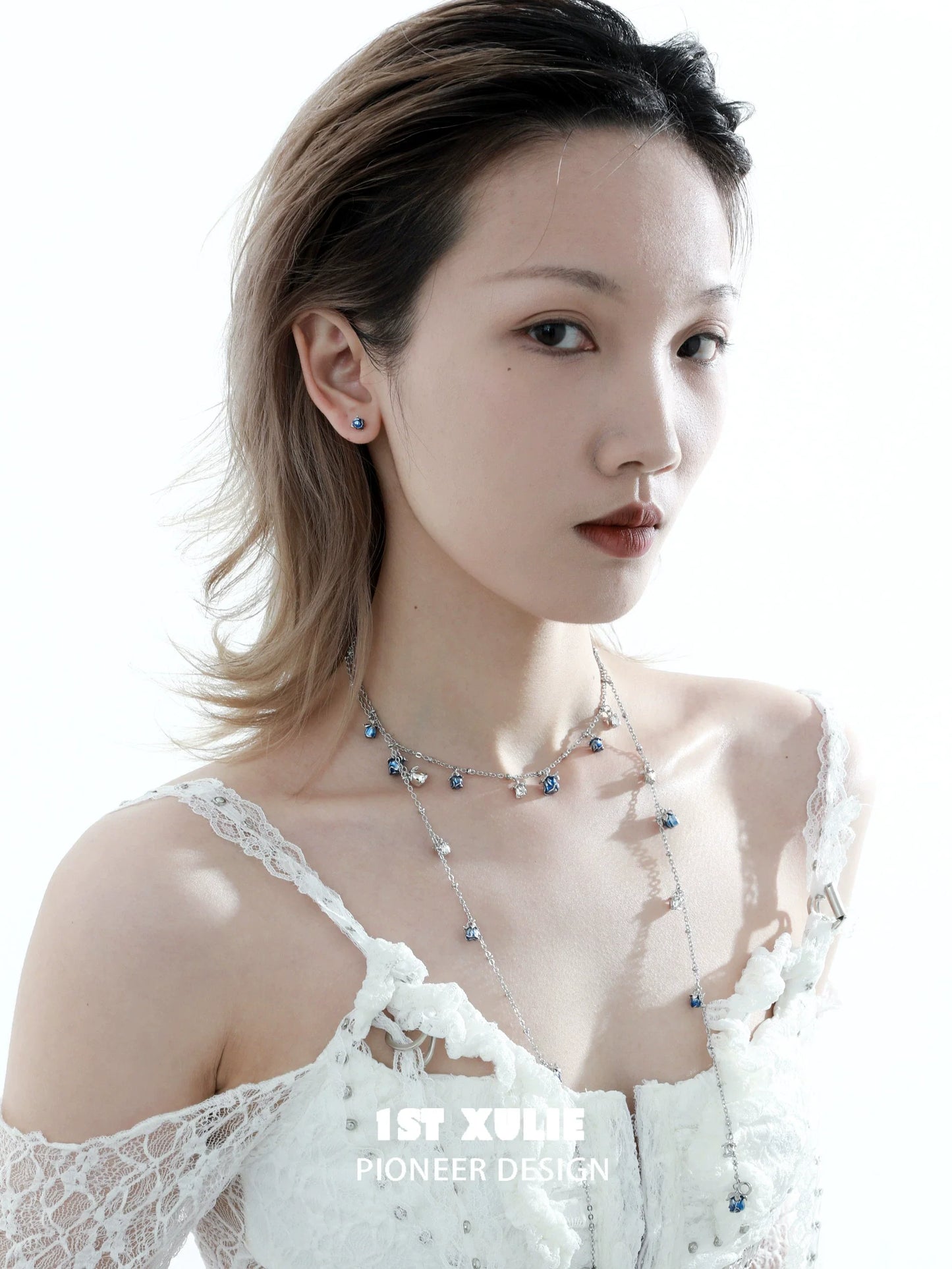 Model wearing crimson and azure rose stud earrings with delicate features and a lace dress