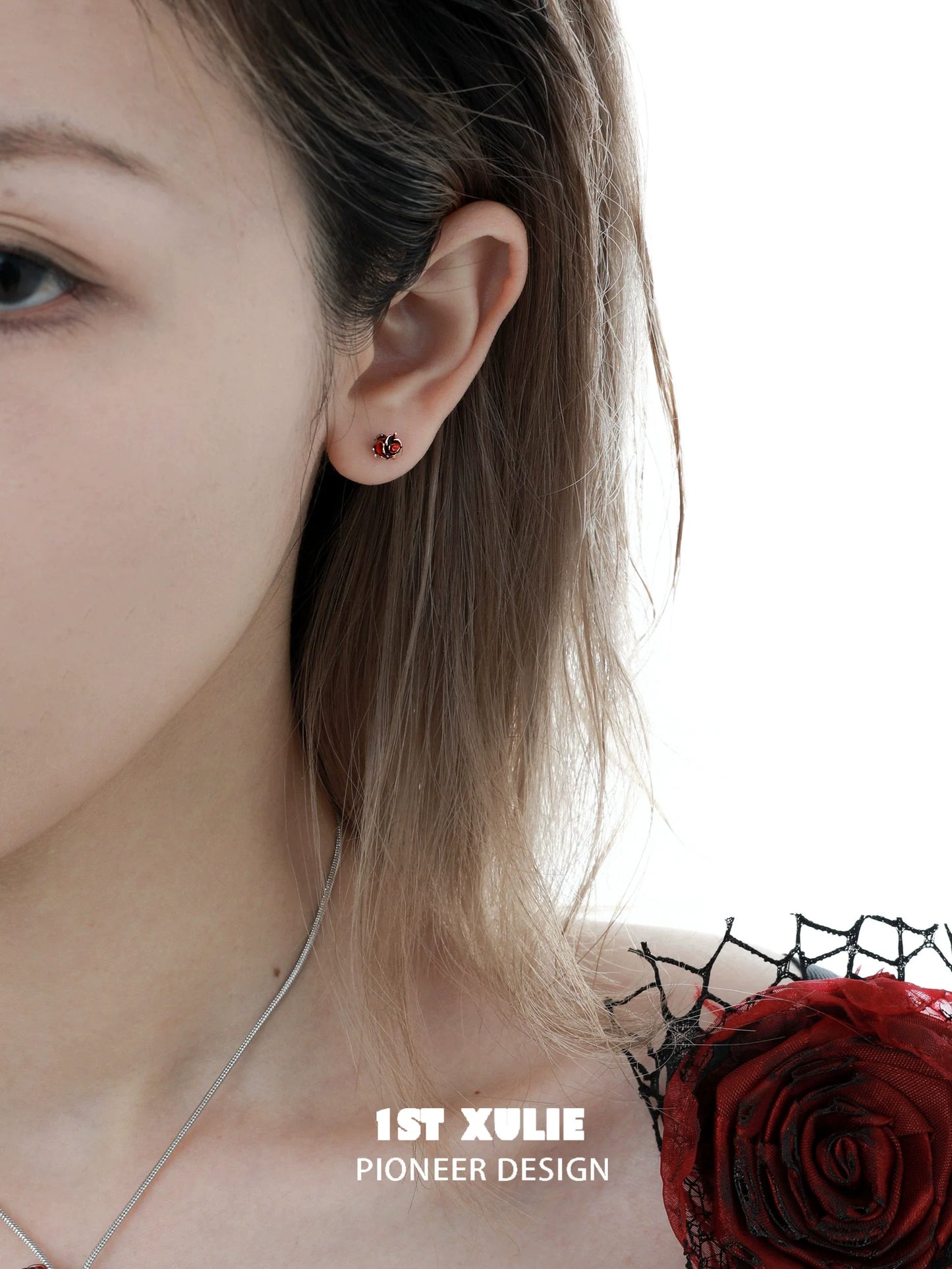 Crimson and azure rose stud earrings showcased on a model's ear with delicate styling