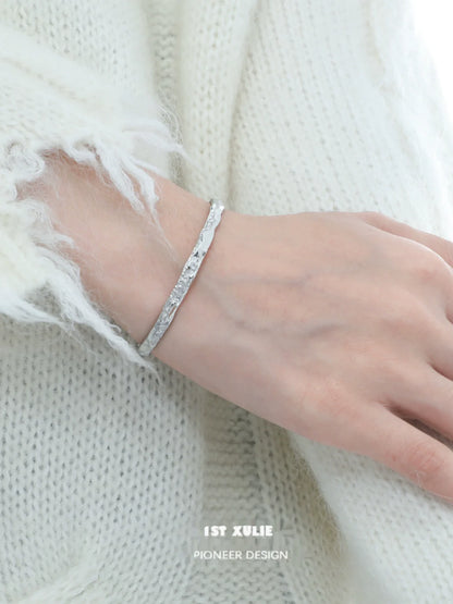 Elegant minimalist silver bracelet displayed on a hand with a cozy knit sweater