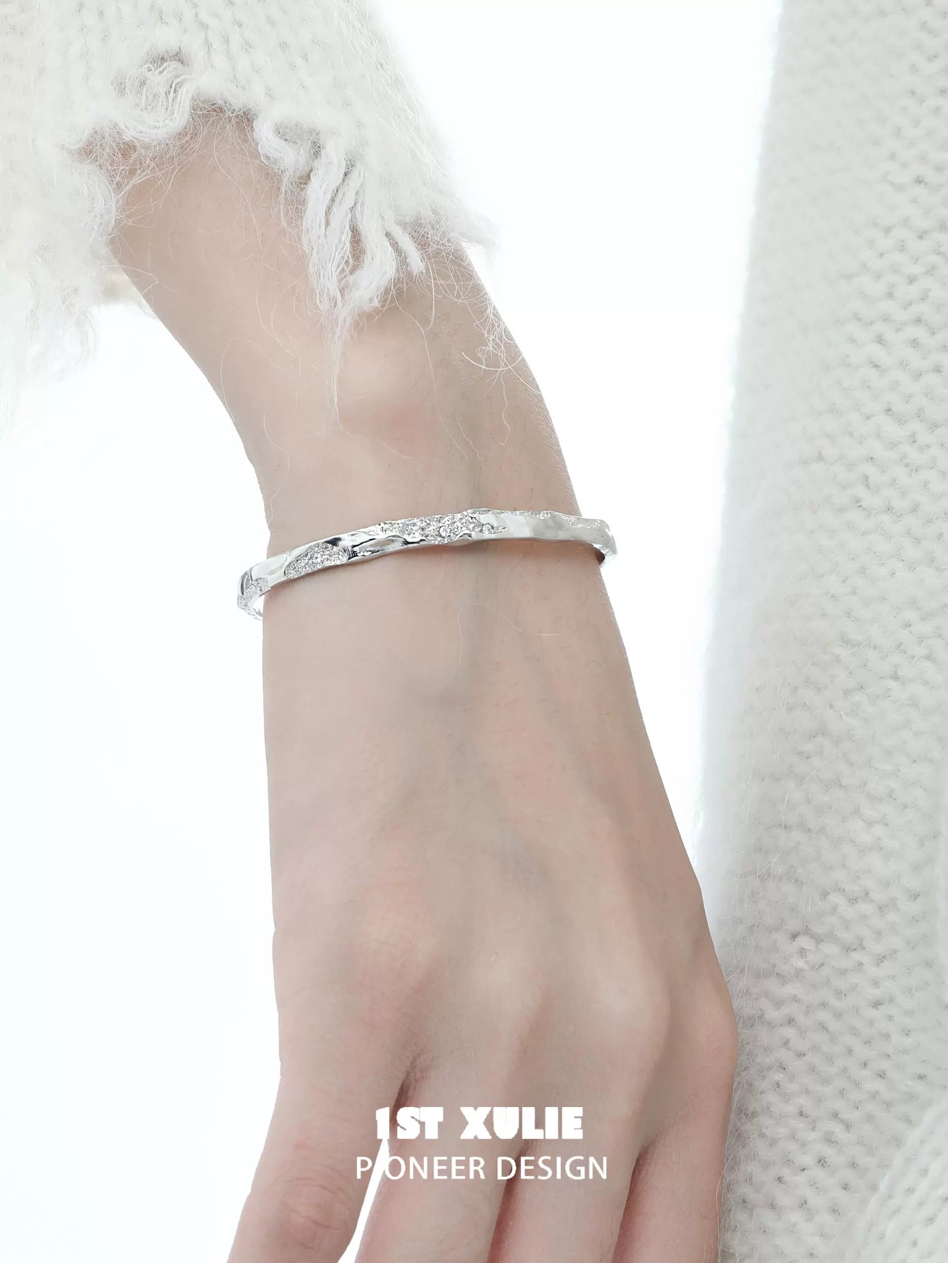 Minimalist silver bracelet from 1ST XULIE displayed on a hand with a soft, textured sweater