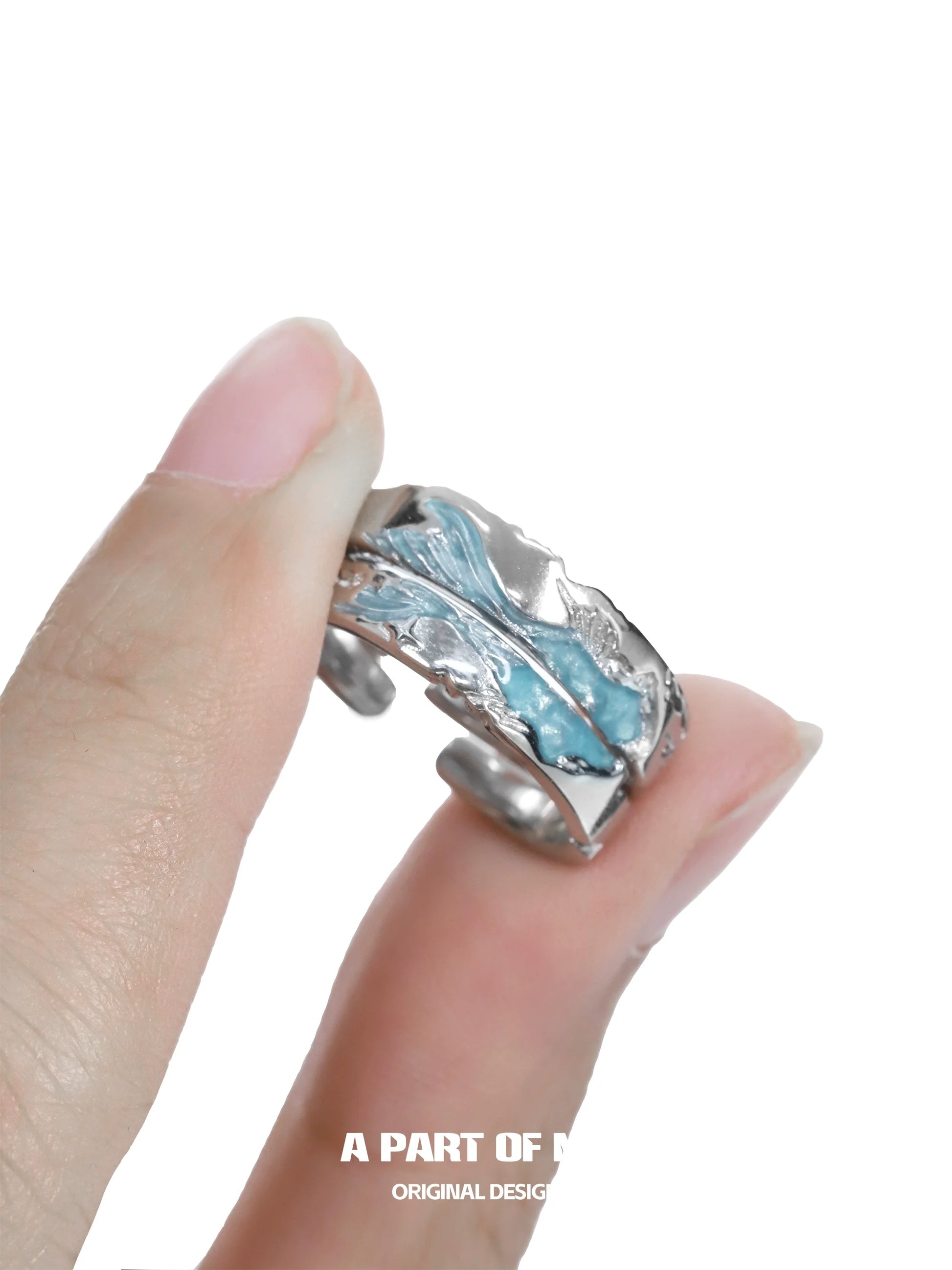 Azure dream fish ring with intricate wave design held between fingers for a unique ocean-inspired look