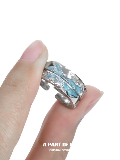 Azure dream fish ring with intricate wave design held between fingers for a unique ocean-inspired look