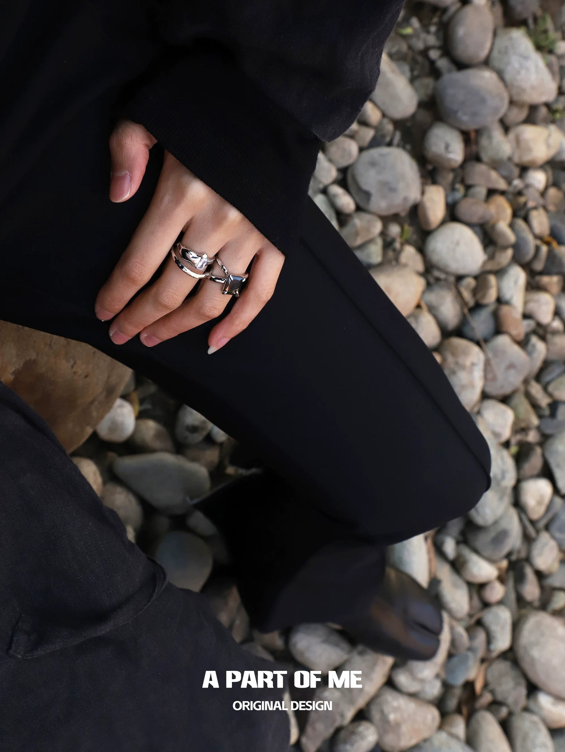 Clear quartz ring displayed on a hand with other unique rings against a rocky background