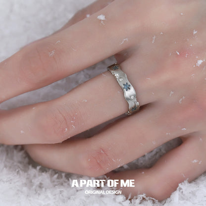 A silver snowflake love ring with delicate blue accents showcased on a hand in snow