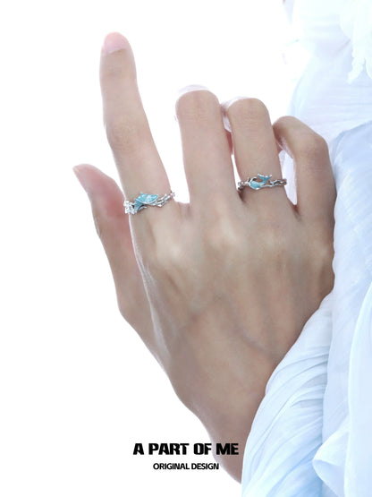 A pair of elegant blue fishtail couple rings shown on a hand with delicate silver accents