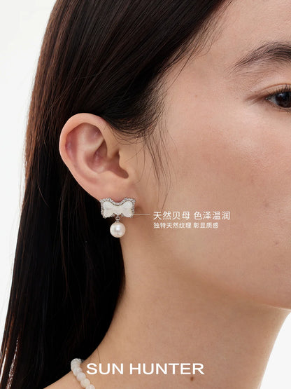 Elegant SUN HUNTER bow pearl earrings featuring a sparkling bow design and a dangling pearl