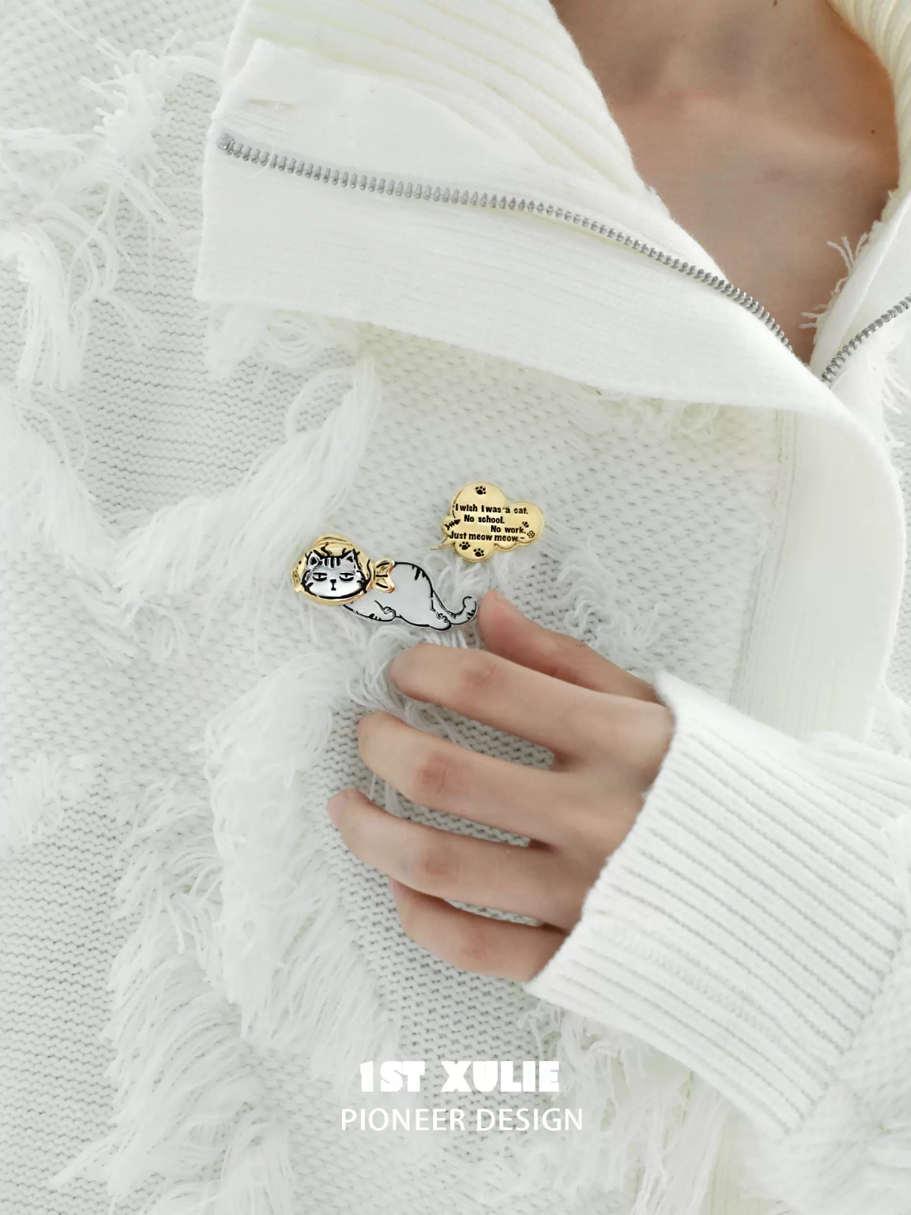 Cute cat silver brooch featuring playful design attached to a white fringed sweater