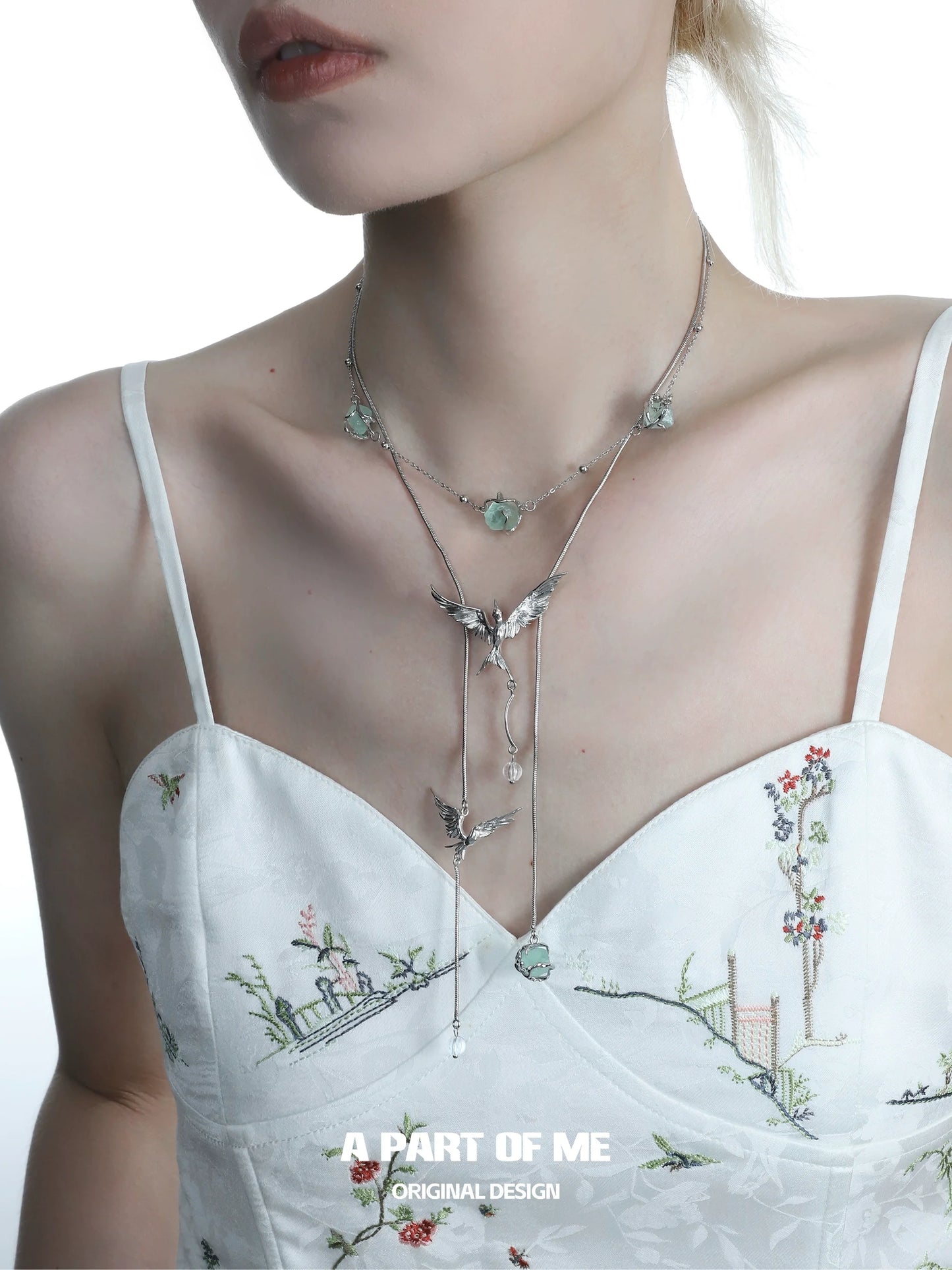 A PART OF ME flying bird fluorite necklace elegantly displayed on a model's neck against a floral outfit