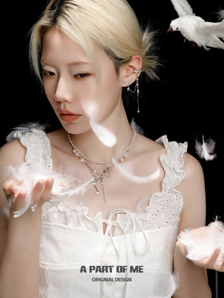 Model wearing a flying bird pearl necklace surrounded by soft white feathers