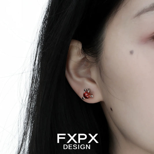 Close-up of bloody dragon claw gothic earrings worn on a person's ear with dark hair