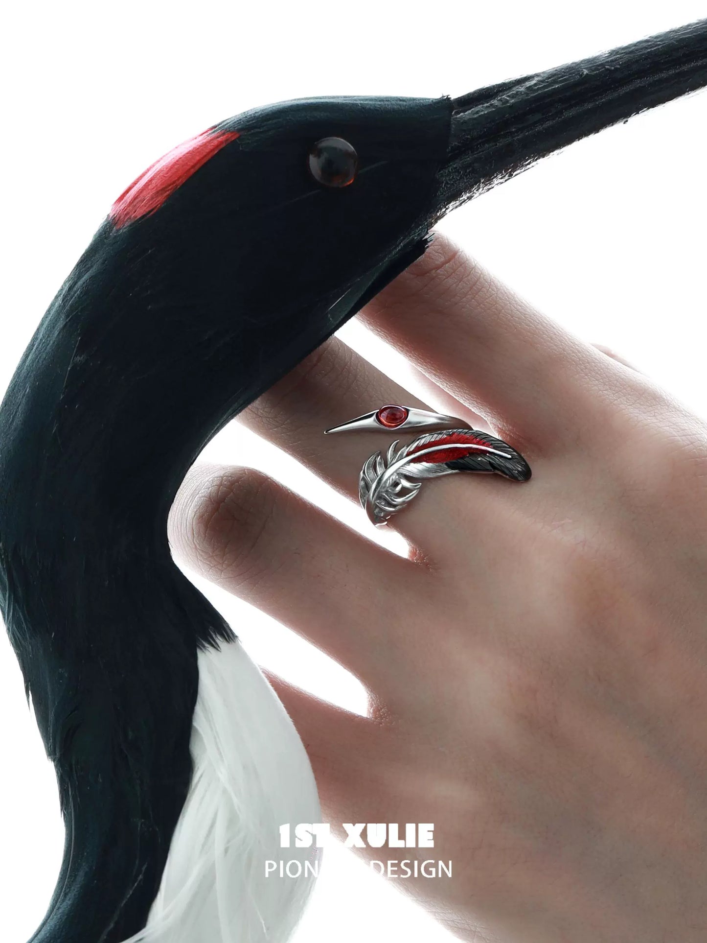 Gothic silver crane ring with a red gemstone, displayed on a model's hand with a crane sculpture