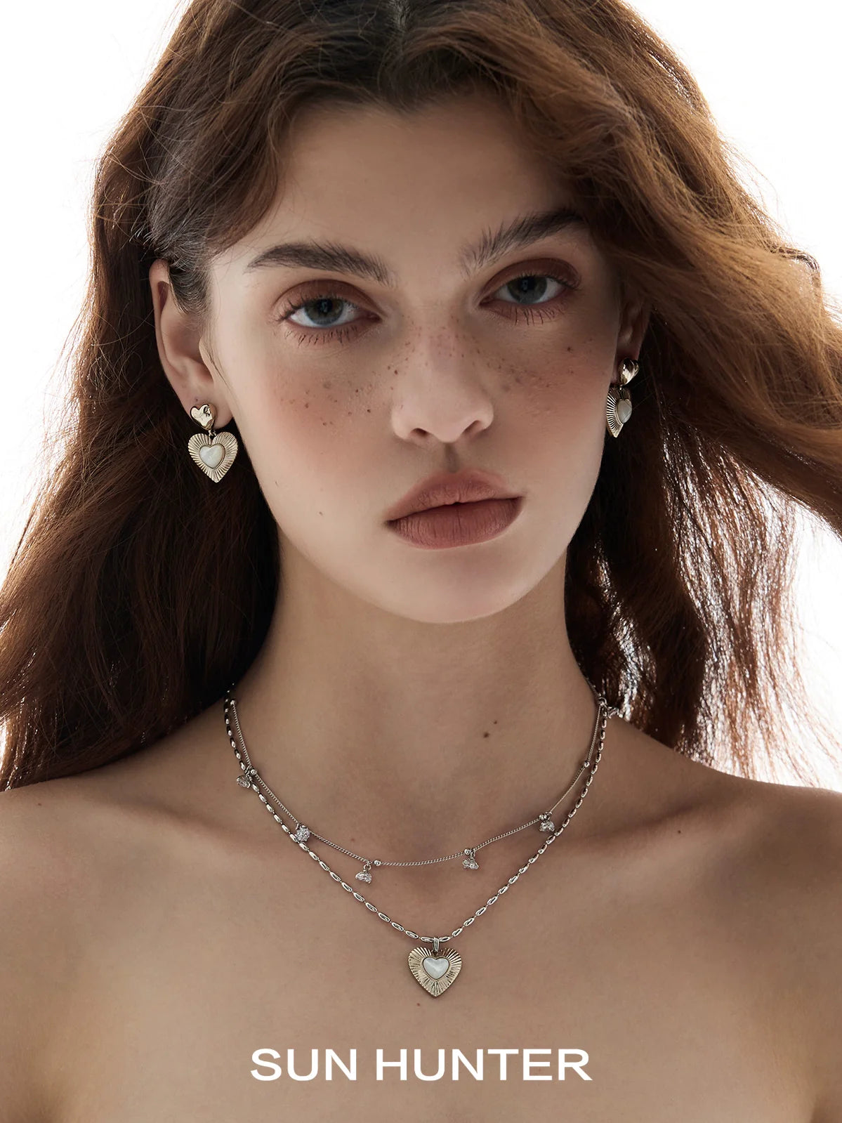 Model wearing heart shaped statement earrings with a layered silver necklace from SUN HUNTER