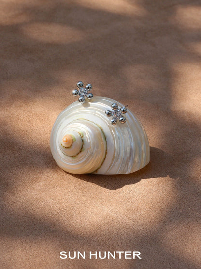 Stylish island flower silver earrings displayed on a decorative seashell background