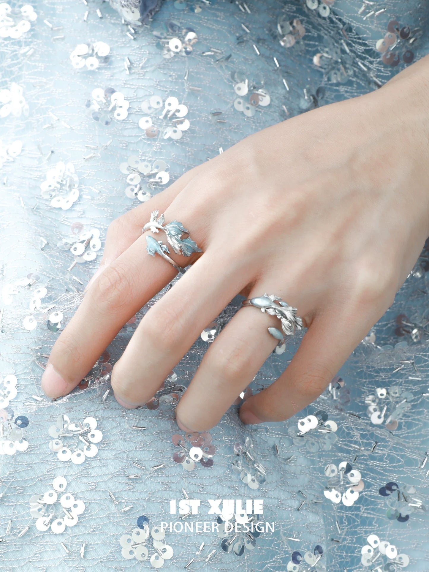 Elegant mermaid tail silver ring featuring intricate detailing, worn on a hand against a sparkling background