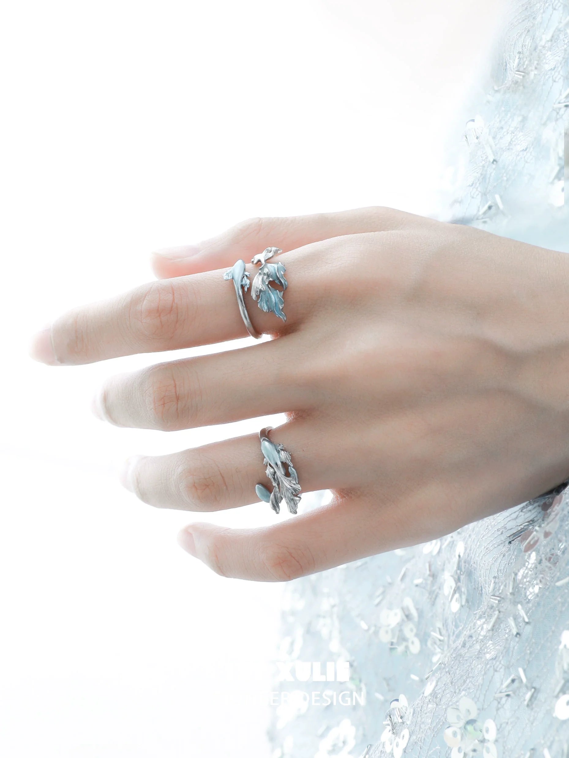 Elegant mermaid tail silver ring featured on a model's hand with a shimmering background