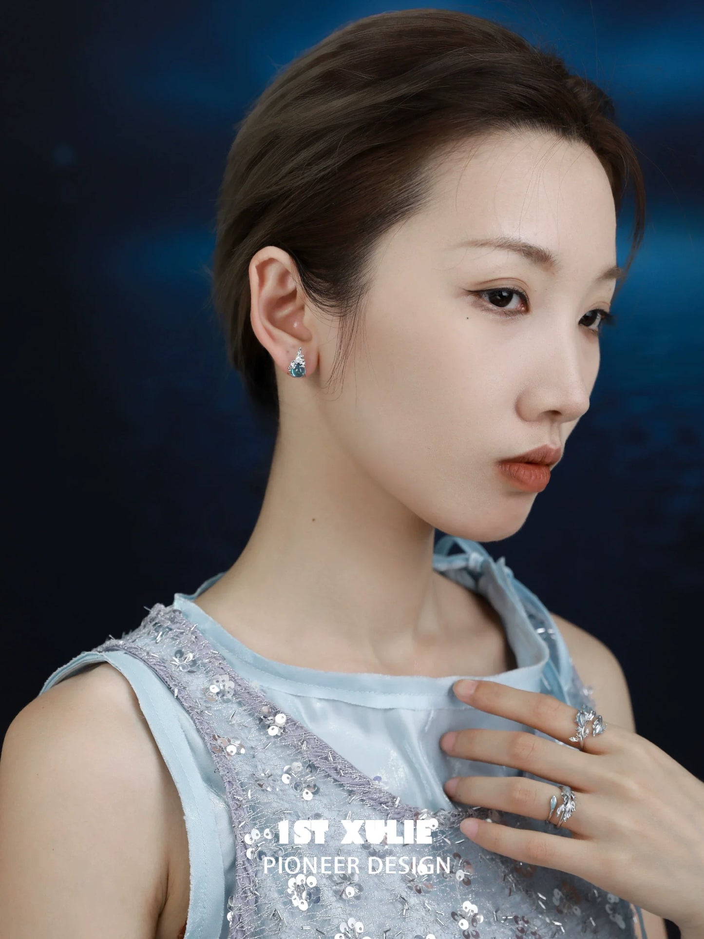 Elegant model displaying mermaid tear earrings with shimmering details against a blue background