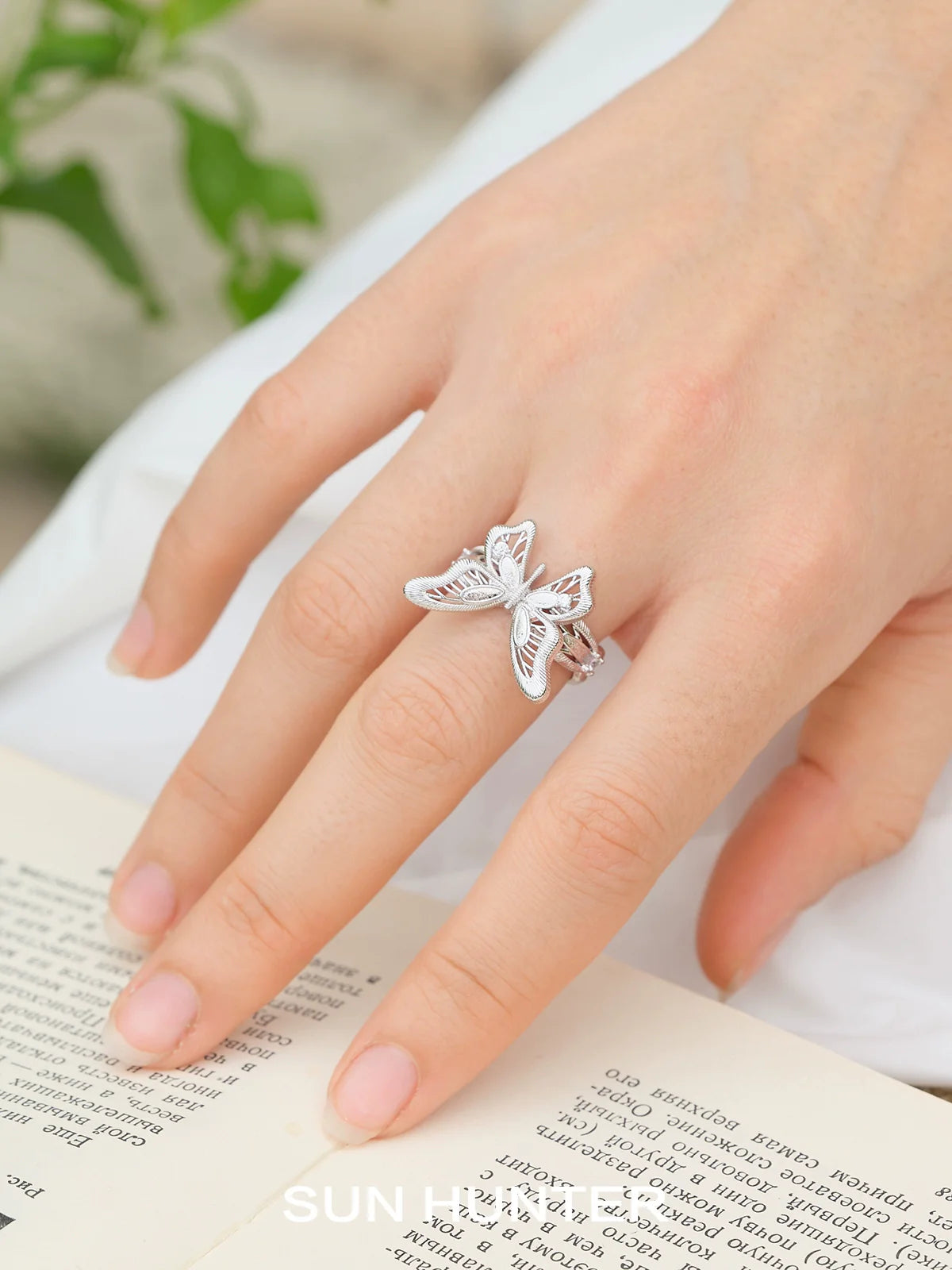 Elegant SUN HUNTER mystic butterfly ring in silver, showcasing detailed butterfly design on a hand with an open book