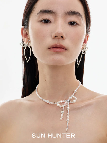 Elegant SUN HUNTER pearl bow ribbon earrings showcased on a model with a pearl necklace