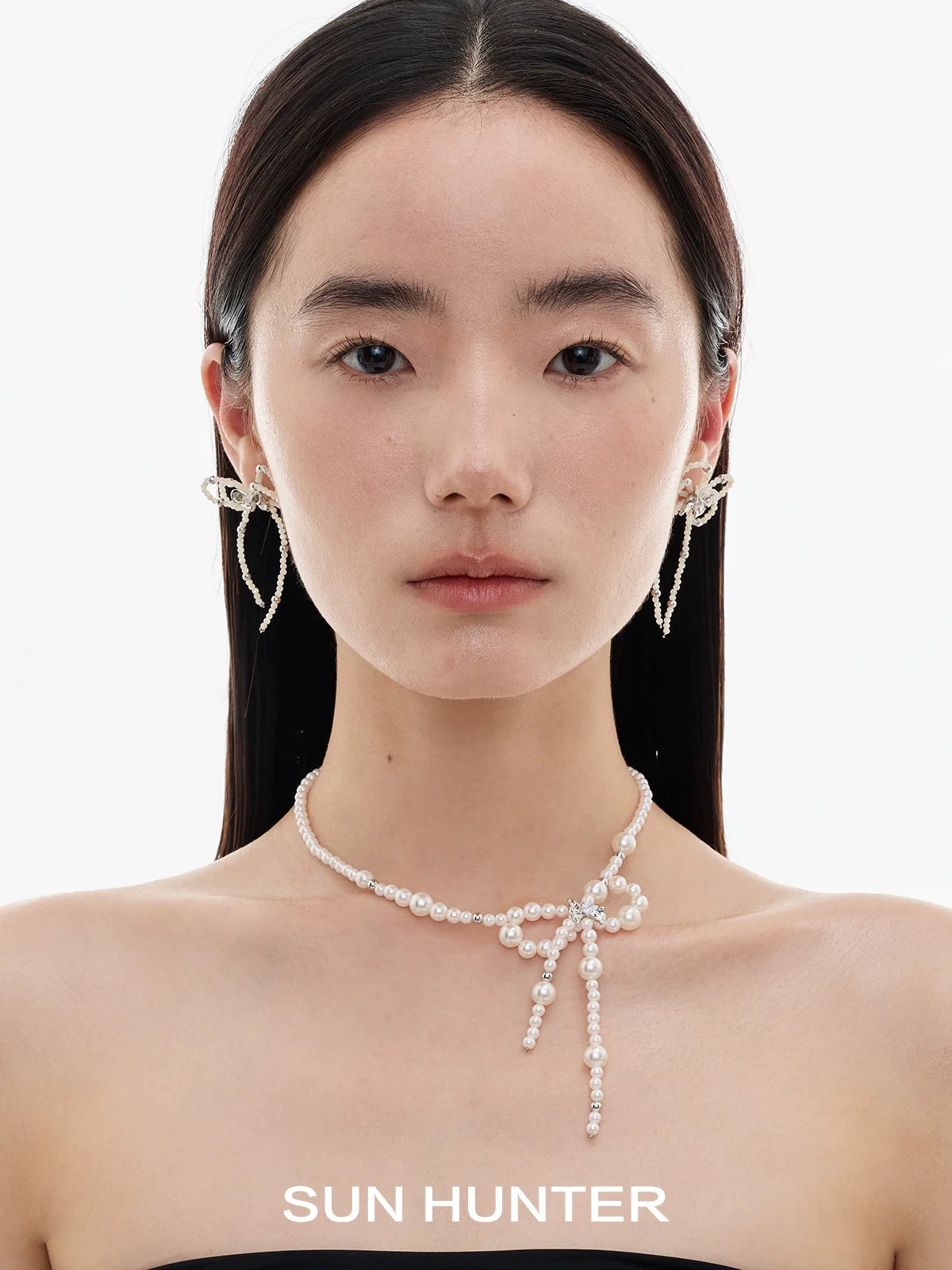 Elegant SUN HUNTER pearl bow ribbon earrings showcased on a model's ears with a simple background