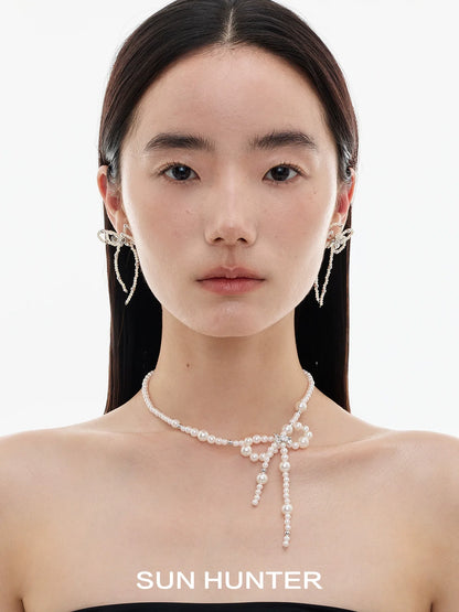 Elegant SUN HUNTER pearl bow ribbon earrings showcased on a model's ears with a simple background