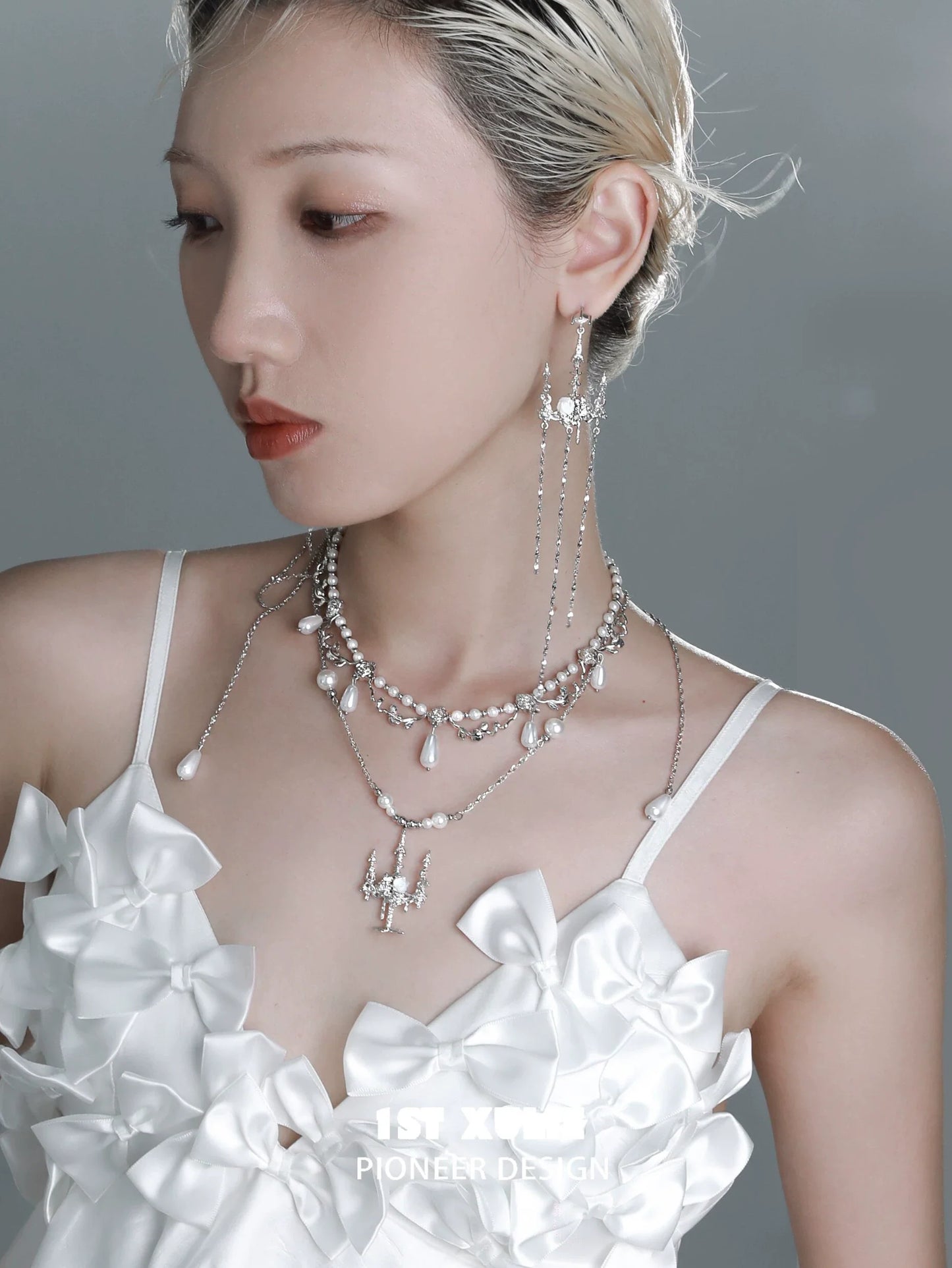 Elegant pearl clavicle necklace layered with silver accents, styled on a model wearing a white outfit