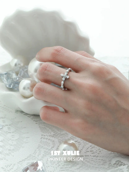 Elegant pearl cross silver ring displayed on a hand with a decorative shell and pearls in the background