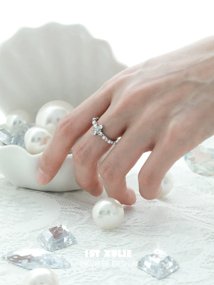 Elegant pearl cross silver ring showcased on a hand amidst decorative pearls and gems