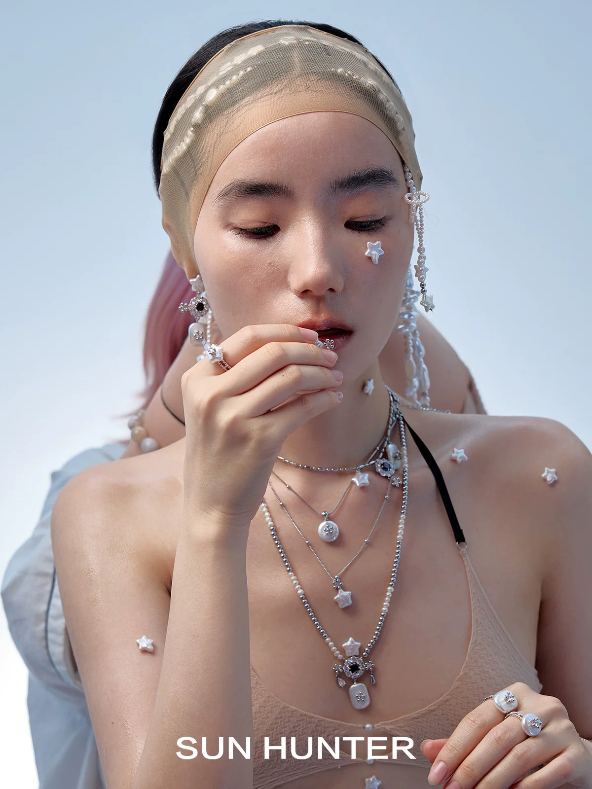 Model wearing SUN HUNTER pearl riddle rings along with layered silver necklaces and accessories