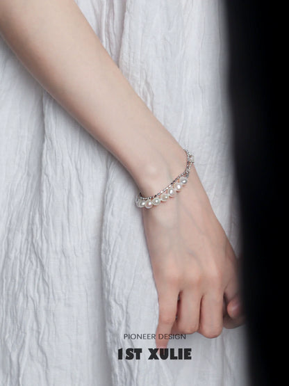 Elegant baroque pearl silver bracelet worn on a hand against a textured white background