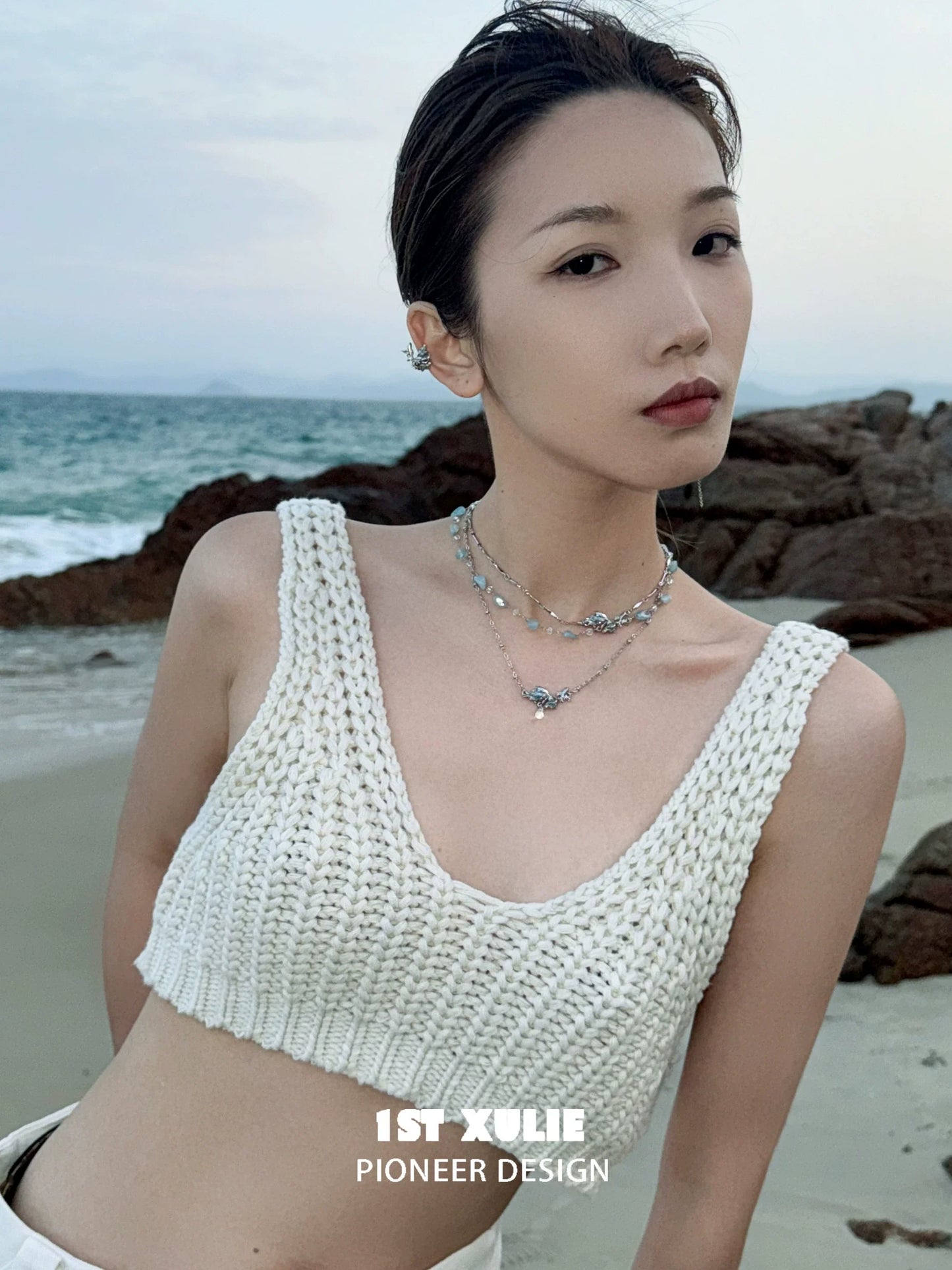 Model wearing a stylish playful fish necklace paired with a white knitted crop top at the beach