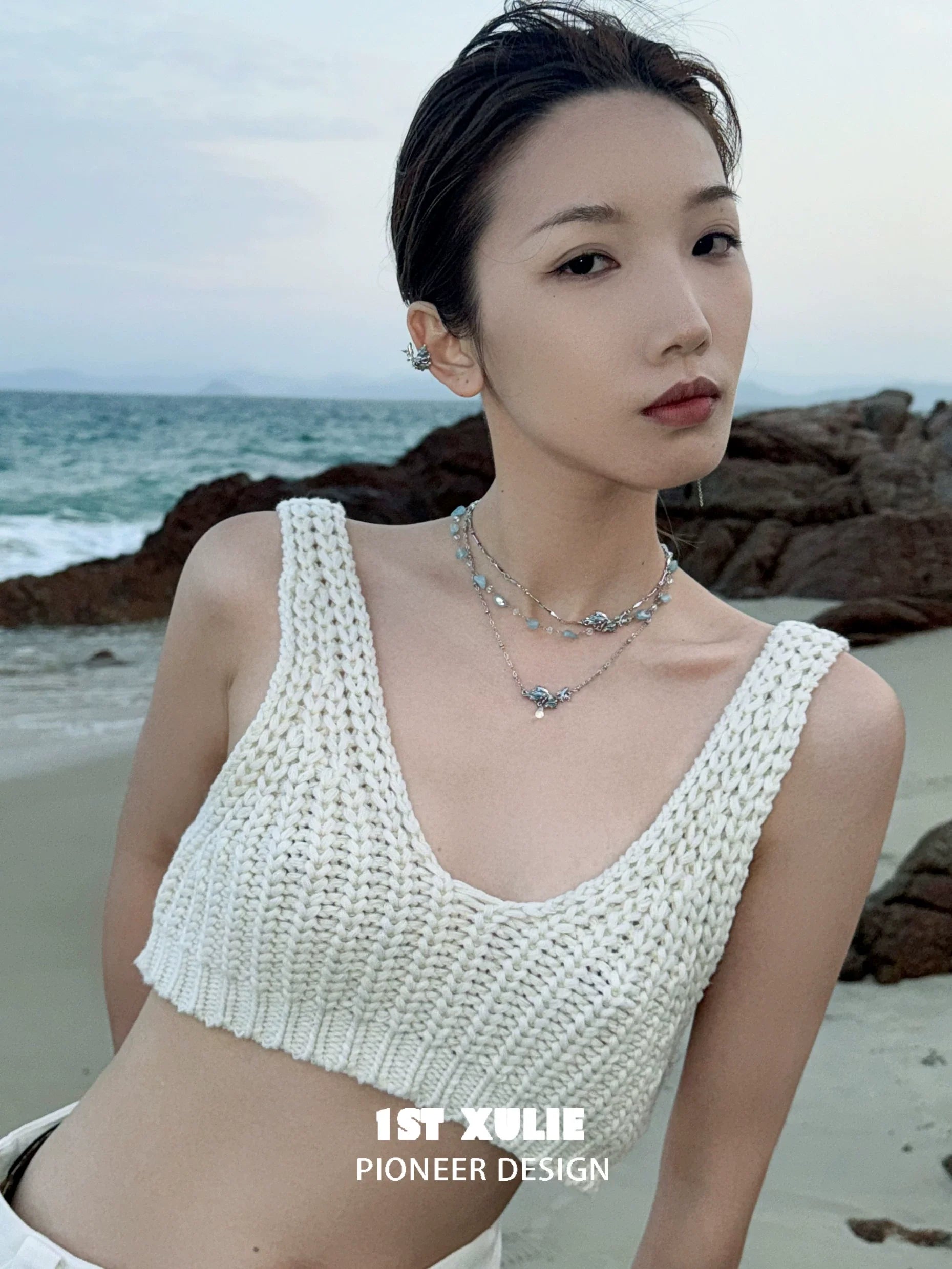 Model wearing a stylish playful fish necklace paired with a white knitted crop top at the beach