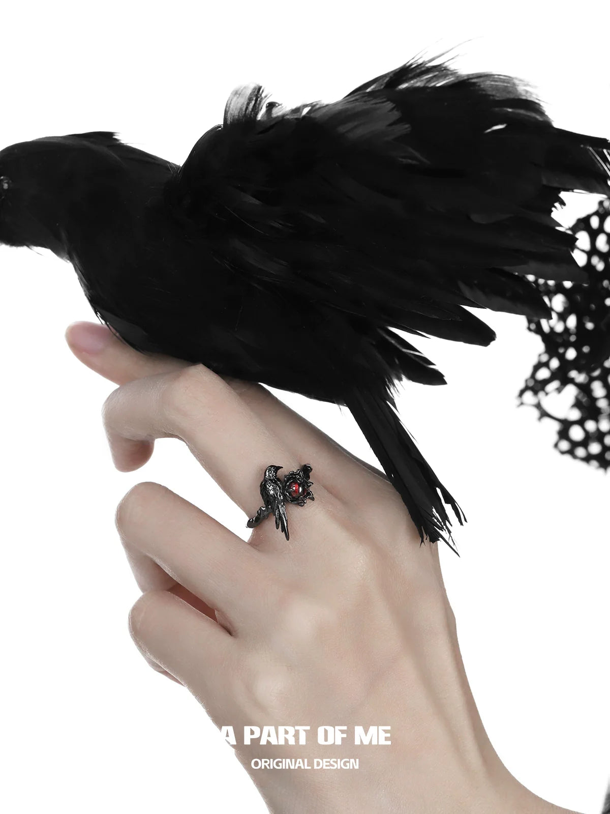 A raven heart ring featuring intricate detailing and a striking design, worn on a finger with a black raven in the background