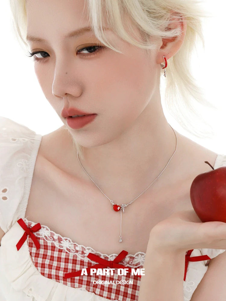 A PART OF ME red apple star necklace elegantly worn with a blouse and holding an apple