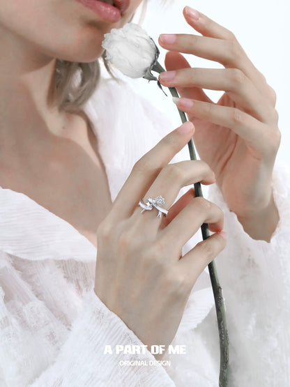 A PART OF ME rose bow silver ring showcased on a hand holding a white rose for a delicate look