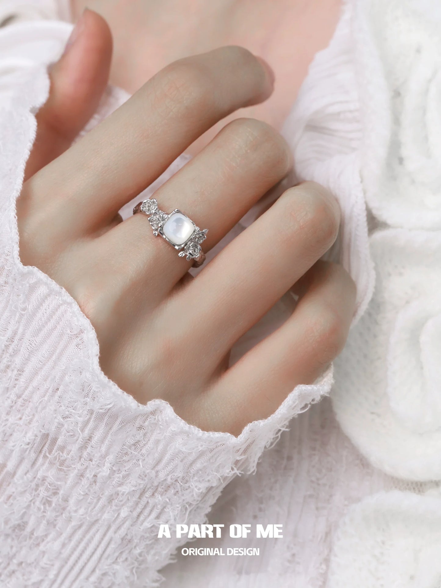 A PART OF ME rose silver ring with a large stone and decorative details worn on a hand with a white sweater