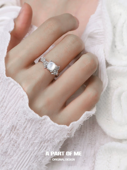 A PART OF ME rose silver ring with a large stone and decorative details worn on a hand with a white sweater