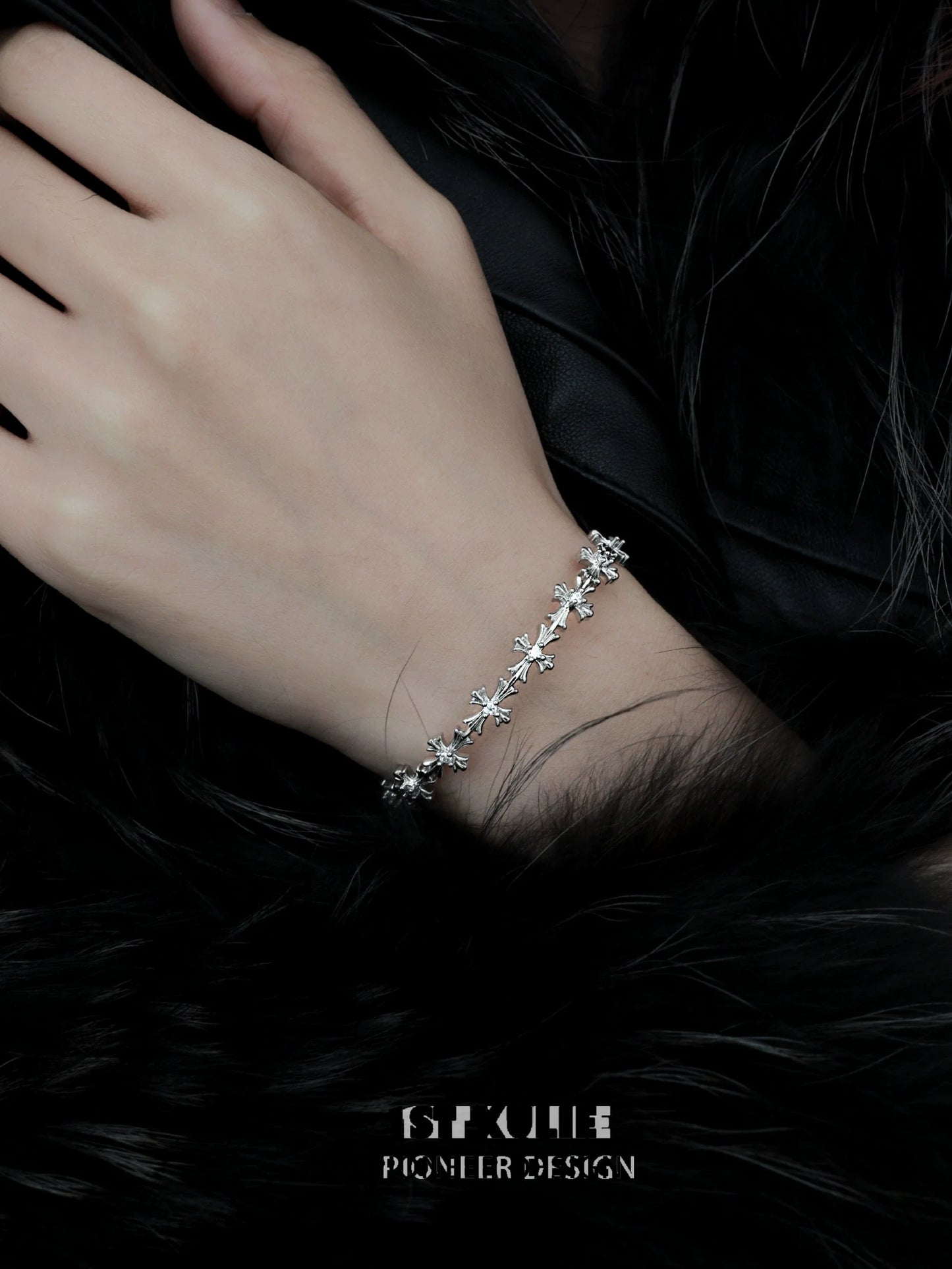 Elegant silver cross bracelet delicately worn on a hand against a dark fur background