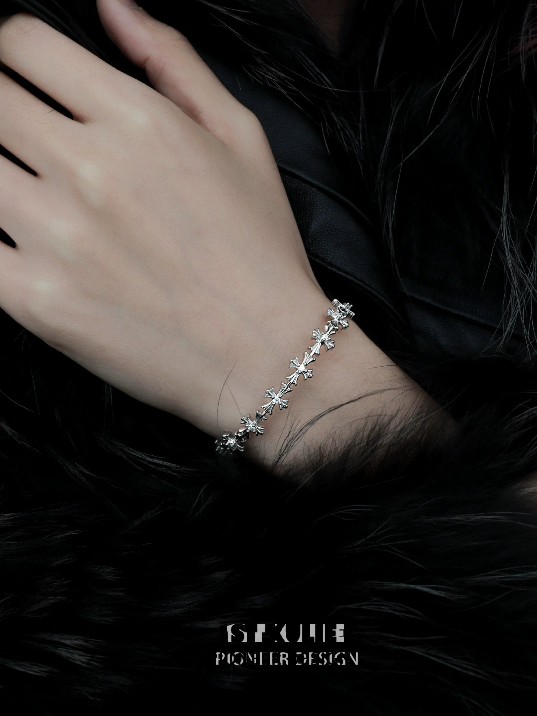 Elegant silver cross bracelet delicately worn on a hand against a dark fur background