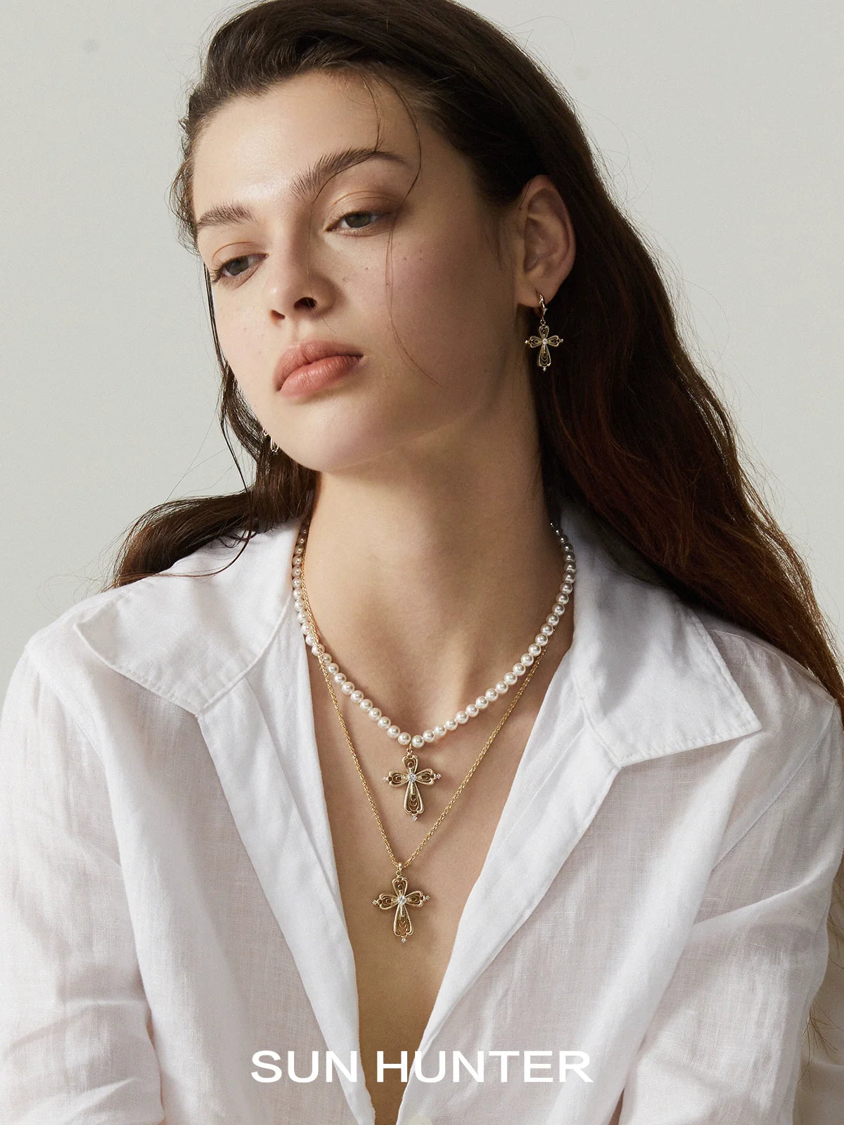 Woman wearing SUN HUNTER teardrop cross necklace layered with pearl necklaces and matching earrings