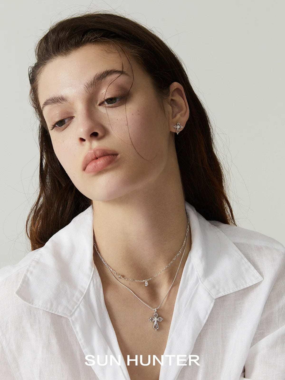 Model wearing a silver teardrop cross necklace layered with delicate jewelry