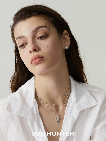 Model wearing a silver teardrop cross necklace layered with delicate jewelry