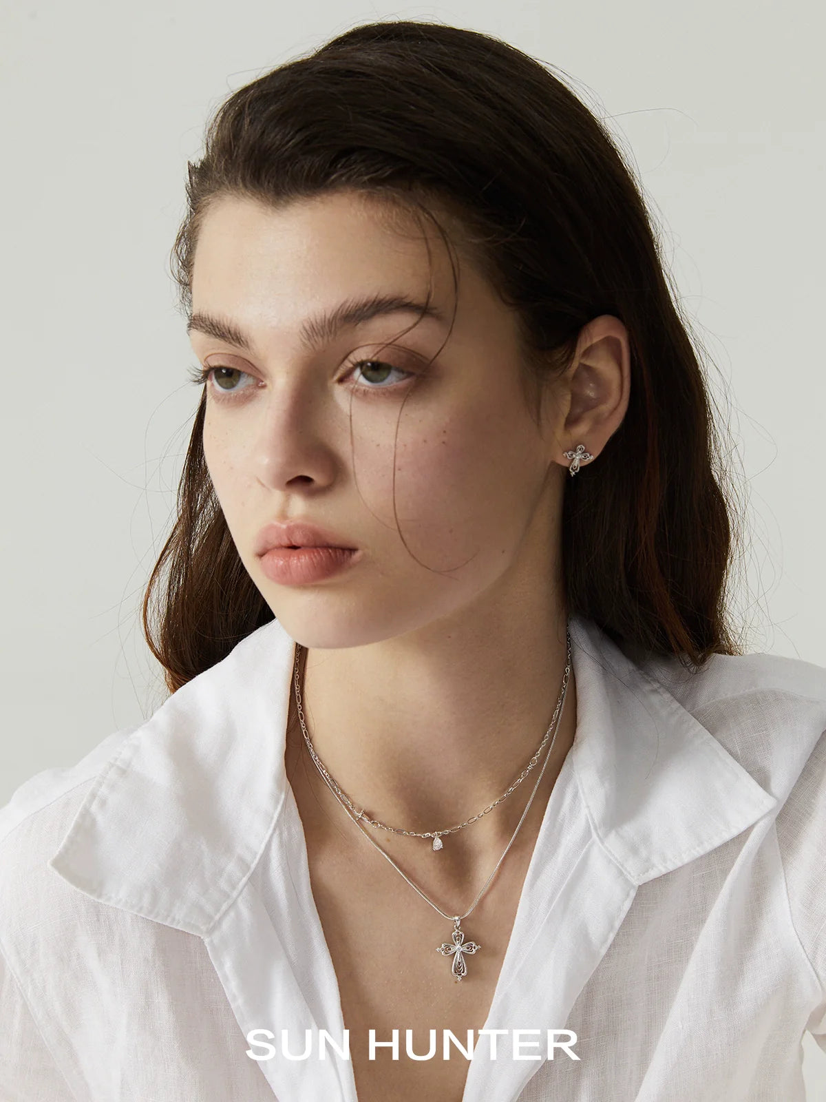 Model wearing a teardrop cross necklace layered with silver chain jewelry for a stylish look