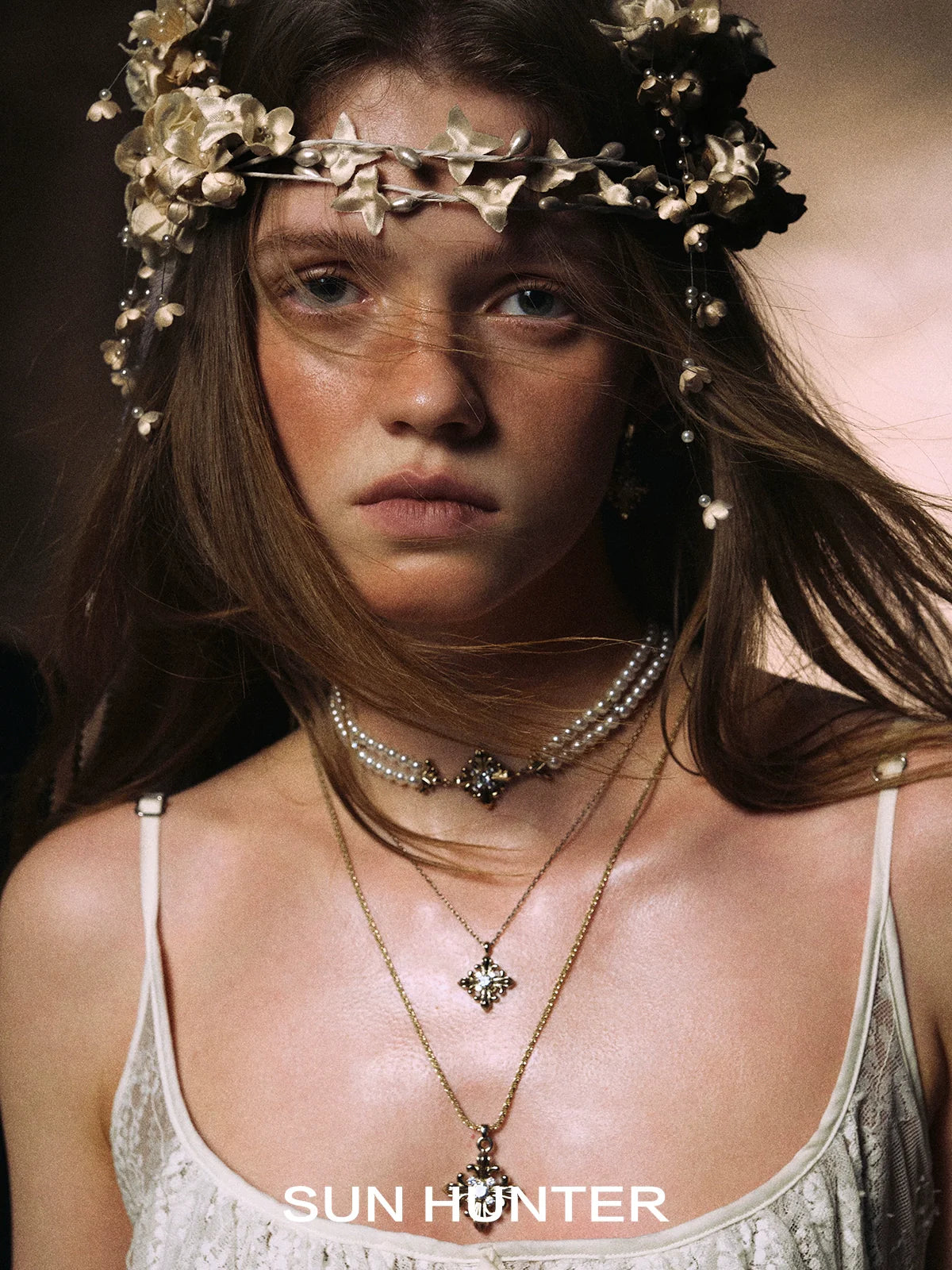 Model wearing SUN HUNTER Twilight Iris braided bracelet with floral headpiece and layered necklaces