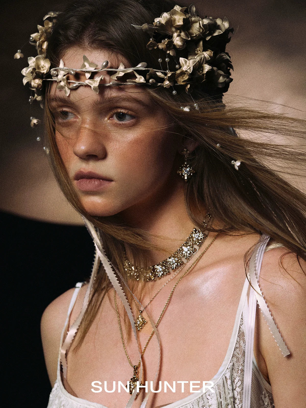 Model wearing unique floral drop earrings from SUN HUNTER with a floral crown and layered necklaces