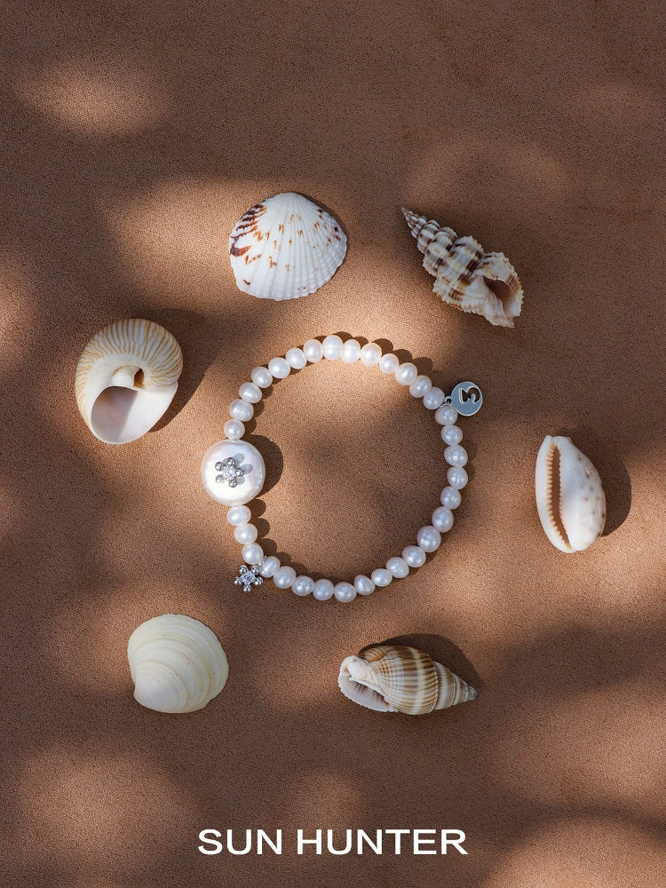 SUN HUNTER unique pearl bracelet displayed among seashells on a sandy surface